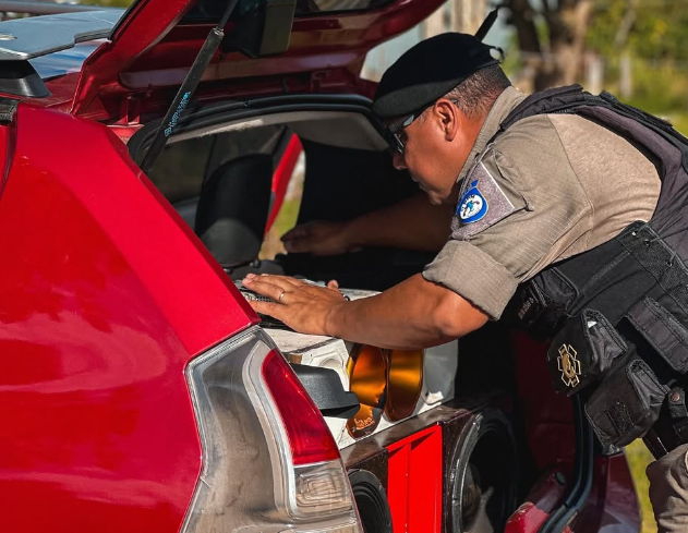 Policial Militar realizando vistoria no porta-malas de um automóvel.